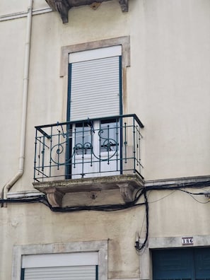 A building with a balcony featuring ornate metal railings, a window with shutters, and a visible pipe. - Refúgio do Barão (Lisboa)