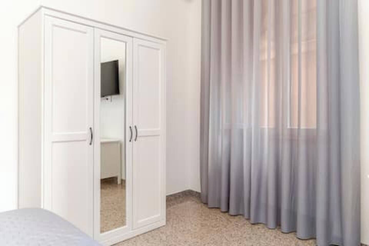 A bedroom with a wardrobe, a bed, and sheer curtains.