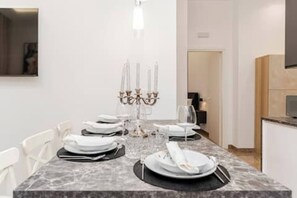 A dining area with a marble table set for four, a chandelier, and a modern kitchen in the background. - The Mazzini Residence (Cosenza)