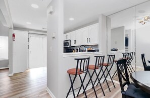 Una cocina moderna con armarios blancos, un microondas y un comedor con sillas negras y una mesa redonda.