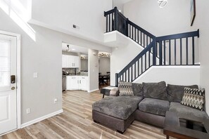 A modern living room with a sectional sofa, a dark staircase, and a kitchen in the background. - Beautiful 3-bedroom townhome with AC in charming Charlotte (Charlotte)