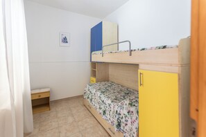 Un lit superposé avec une tête de lit en bois, une armoire jaune et une petite table de chevet en bois.
