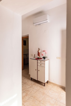 A room with a white cabinet, an air conditioning unit, and a small statue on top.