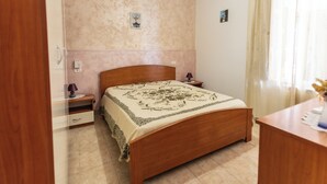 Un dormitorio con una cama de madera, una mesita de noche, una lámpara y un interruptor de luz en la pared.