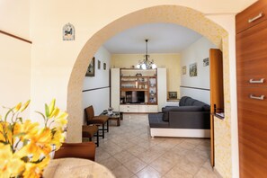 A living room with a sofa, a dining table, and chairs, an arched doorway leading to another room, and a chandelier. - Appartamento Zumbo (Vigliatore)