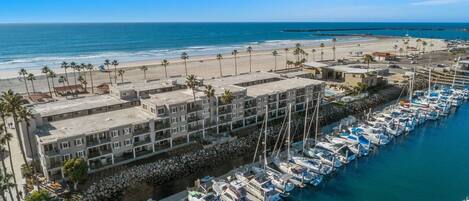 Un hôtel en bord de mer, avec plusieurs étages, une marina remplie de bateaux et une plage en arrière-plan.