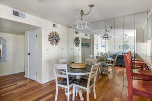 A modern dining area with a round table, white chairs, and a chandelier. - Beachfront 2BR Harbor Condo w/ Ocean View Balcony (Oceanside)