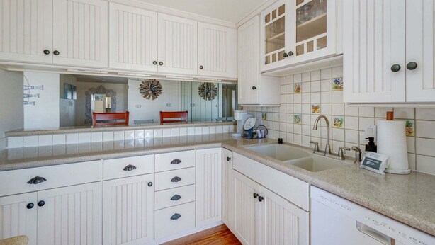 Una cucina con mobili bianchi, un lavello doppio e un rivestimento decorativo.