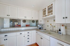 A kitchen with white cabinets, a double sink, and a decorative backsplash. - Beachfront 2BR Harbor Condo w/ Ocean View Balcony (Oceanside)