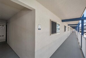 Ein Korridor mit einer Reihe von Fenstern, einem Schild mit der Zimmernummer 212A und einem blauen Geländer auf der rechten Seite.
