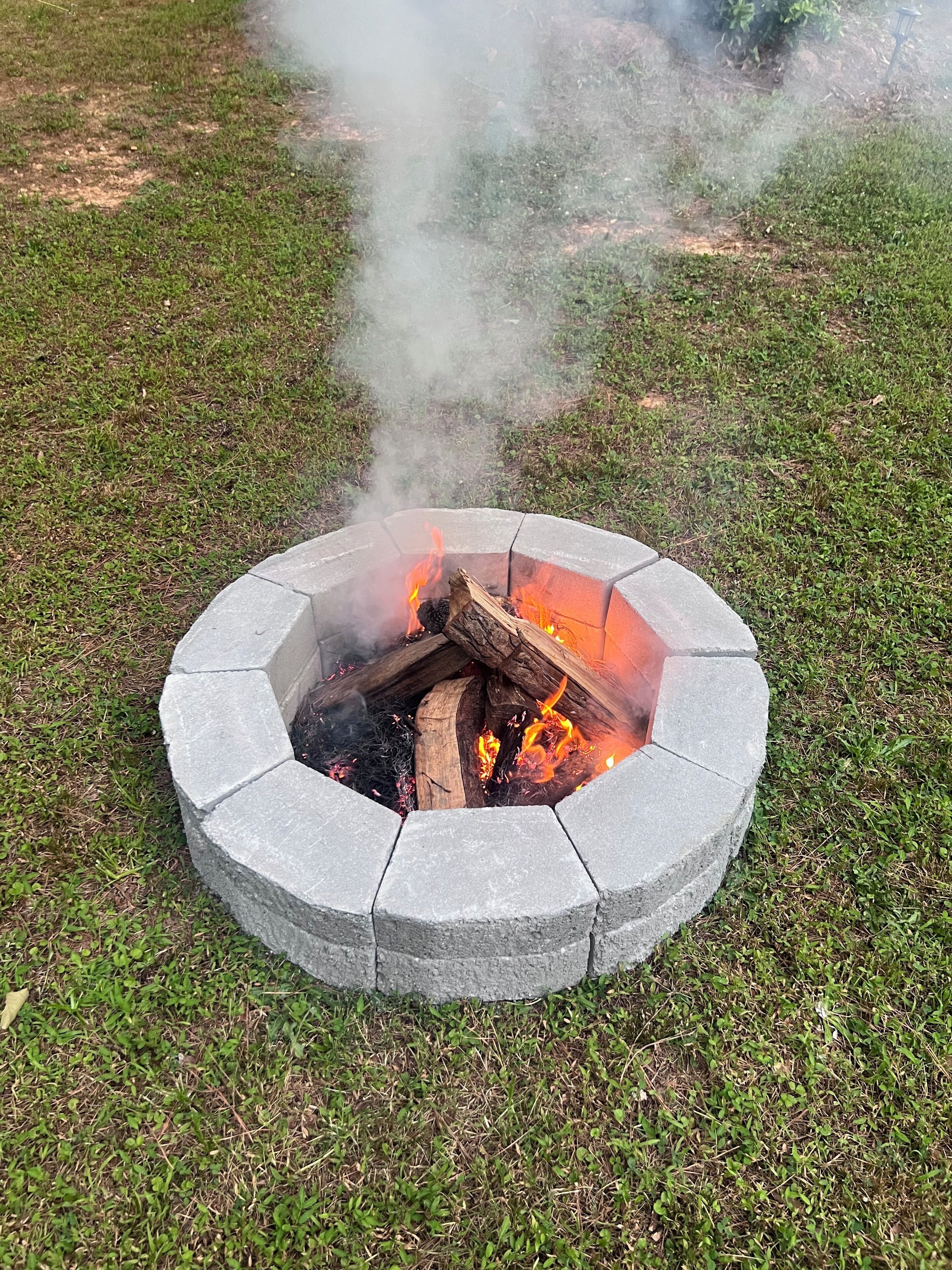 A circular stone fire pit with burning logs and smoke.