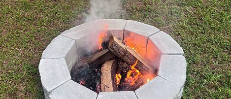 A circular stone fire pit with burning logs and smoke.