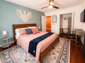 A bedroom with a bed, a ceiling fan, a nightstand, a lamp, a chair, a desk, and a door leading to another room. - Atlanta Oasis with a Spa Suite, Huge Backyard, Fire Pit & Hammocks (Atlanta)