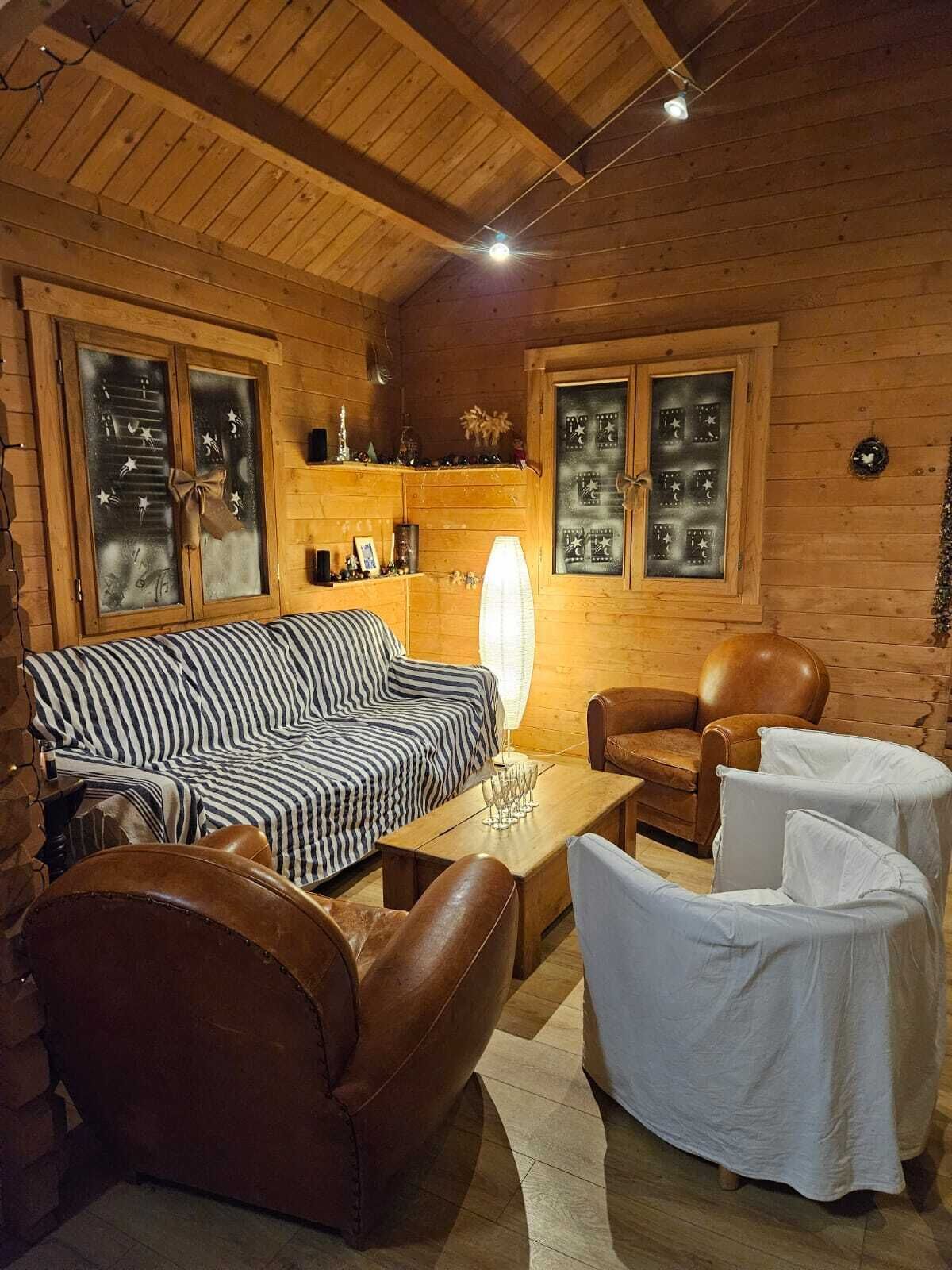 L’intérieur d’un chalet confortable, avec des murs en bois, un canapé à rayures, des fauteuils en cuir, une table basse en bois et une lampe.