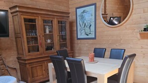 Een houten interieur met een eettafel, stoelen, een kast en een ronde spiegel aan de muur.