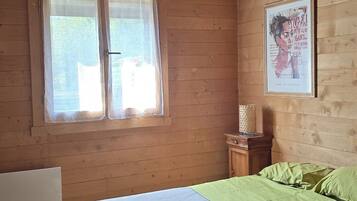 Een slaapkamer in een houten blokhut, met een bed, een raam en een lijst met een foto aan de muur.