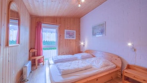 Ein Zimmer mit zwei Betten, Holzboden, einem mit Vorhängen versehenen Fenster und einer Wandleuchte.
