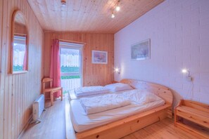 A room with two beds, a wooden floor, a window with curtains, and a wall-mounted light fixture. - Geraumiger Doppelbungalow mit Terrasse und Garten im Ferienpark Mirow (Mirow)