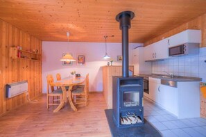 A wooden interior with a dining table, chairs, a kitchen with a stove, and a microwave. - Geraumiger Doppelbungalow mit Terrasse und Garten im Ferienpark Mirow (Mirow)