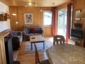 A cozy room with a plaid sofa, a wooden table, and a television mounted on the wall. - Geraumiger Doppelbungalow mit Terrasse und Garten im Ferienpark Mirow (Mirow)