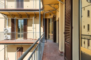 A narrow corridor with a balcony on the left, a door on the right, and a window with shutters. - Irnerio Apts - Olive Green by Wonderful Italy (Bologna)