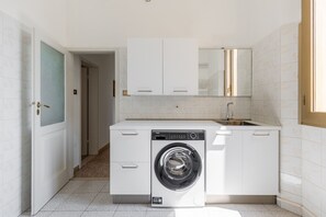 A compact laundry room with a front-loading washing machine, a sink, and white cabinetry. - Irnerio Apts - Olive Green by Wonderful Italy (Bologna)