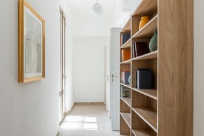 A hallway with a wooden bookshelf, a framed picture on the wall, and a door leading to another room. - Irnerio Apts - Olive Green by Wonderful Italy (Bologna)