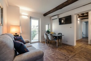 Ein modernes Wohnzimmer mit einer Couch, einem Esstisch mit Stühlen, einem an der Wand montierten Fernseher und Holzboden.