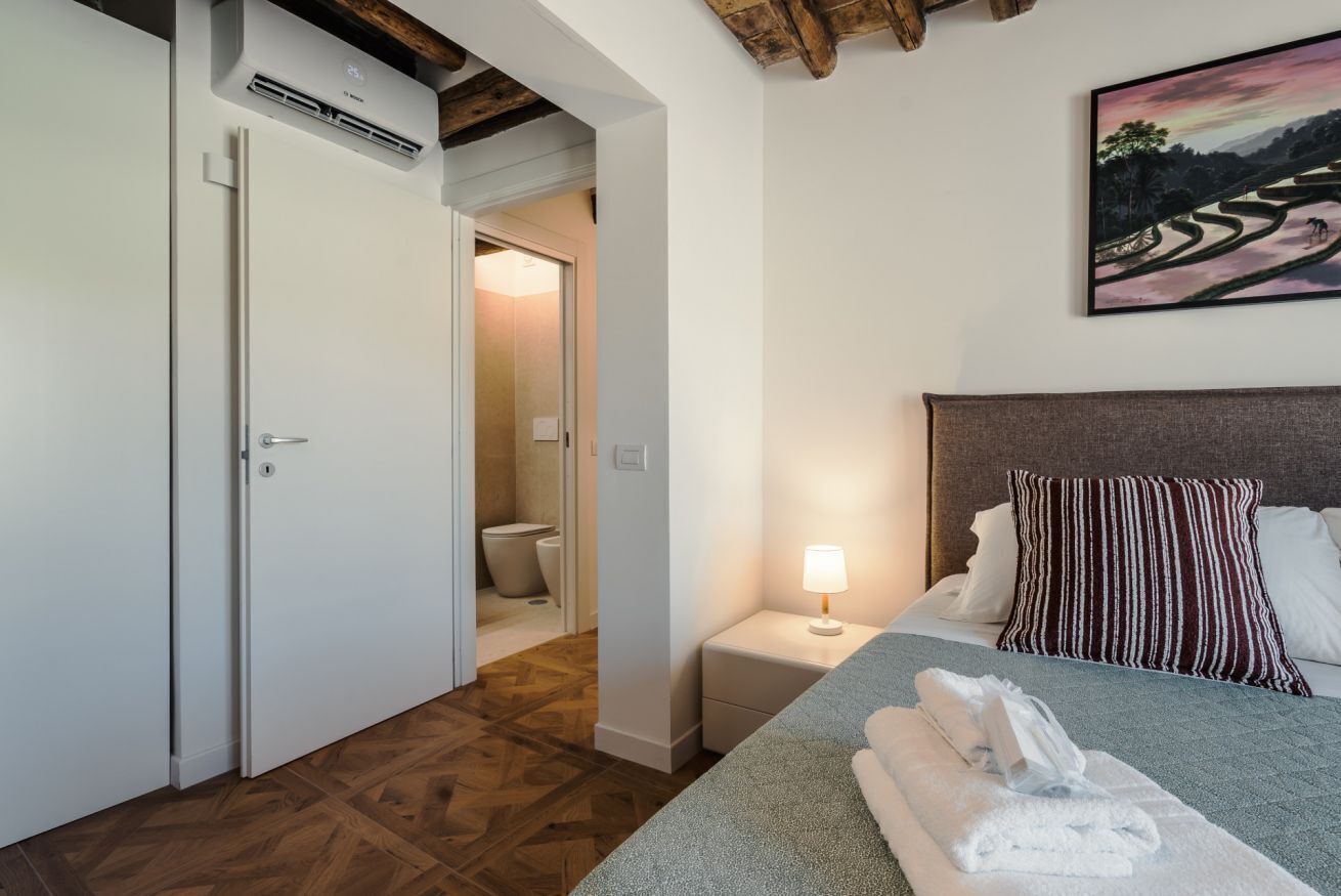 Ein Hotelzimmer mit einem Bett, einem Nachttisch mit Lampe, einem Bild an der Wand und Holzboden.
