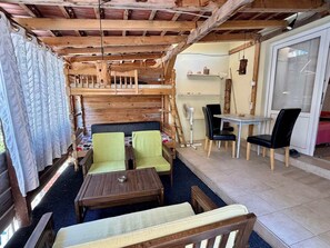 A cozy cabin-style room with a wooden ceiling, a bed with a headboard, two green chairs, a small table, a dining table with chairs, and a fan. - Blue Horizon - Plavi horizonti (Bigova)