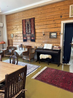 Una sala de estar acogedora con una pared de madera, un piano, una mesa de comedor con sillas y una chimenea.