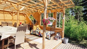 A wooden deck with a table and chairs, a hanging flower pot, and a window overlooking greenery. - Yöveden Ateljeekoti (Mikkeli)