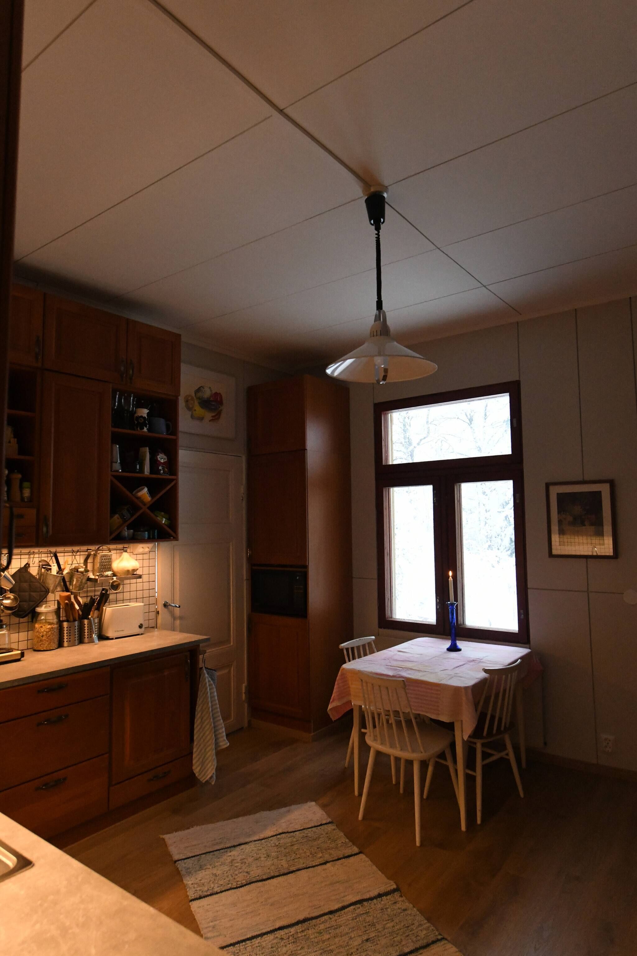 A kitchen with wooden cabinets, a dining table with chairs, a hanging light fixture, and a window with a candle.