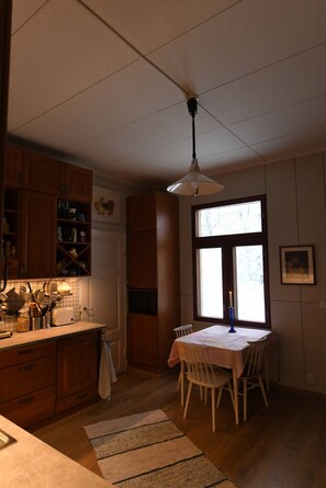 A kitchen with wooden cabinets, a dining table with chairs, a hanging light fixture, and a window with a candle.