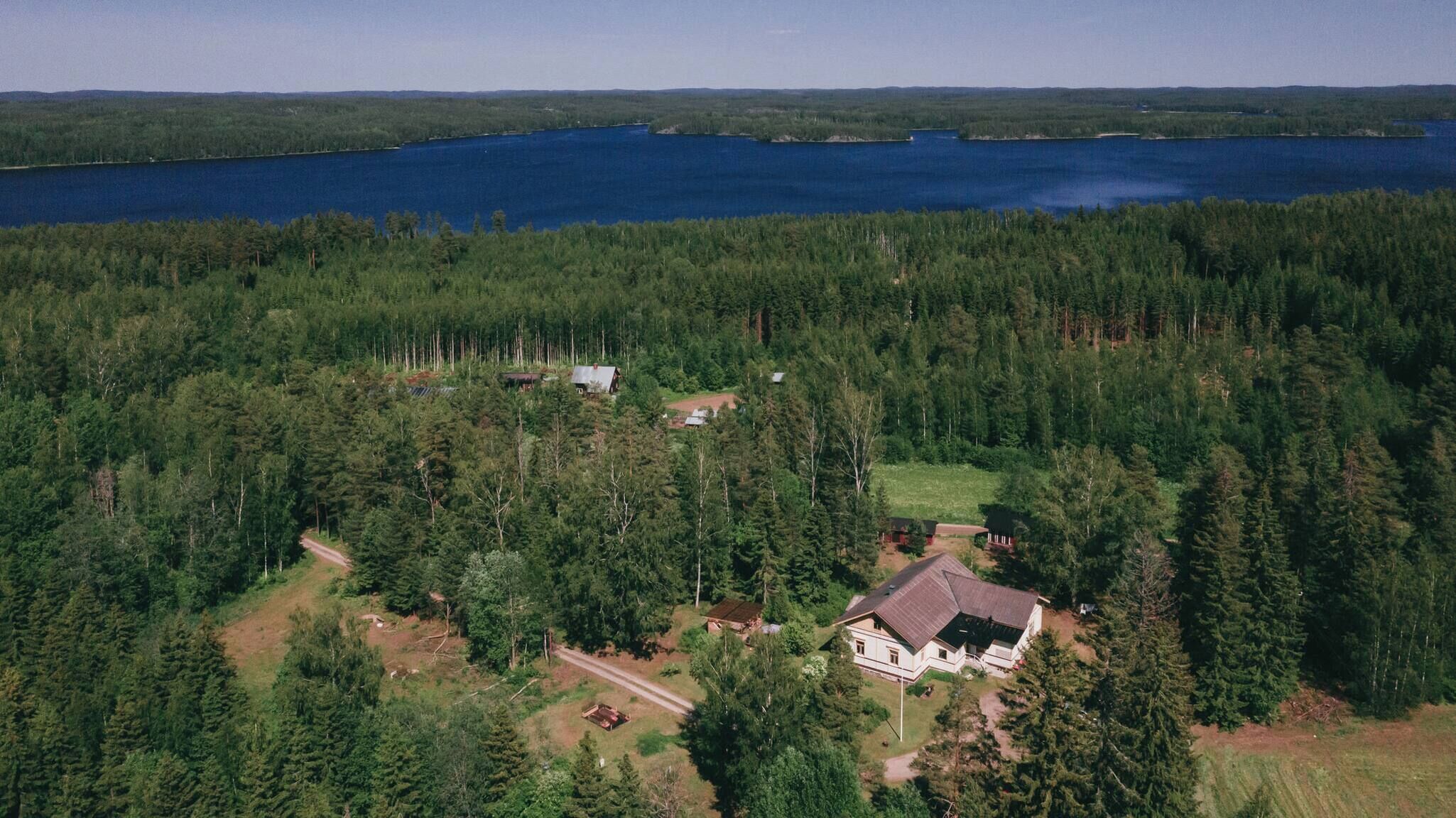 Metsäinen alue, jossa on järvi, talo ja pieni avoin paikka.