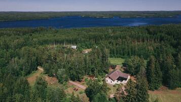 Metsäinen alue, jossa on järvi, talo ja pieni avoin paikka.