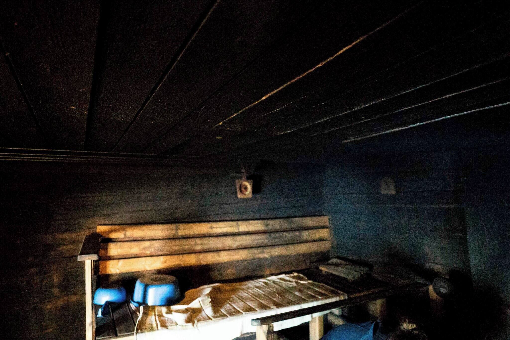 Een kamer in gedempt licht met een houten bank, een tafel en een blauwe stoel.