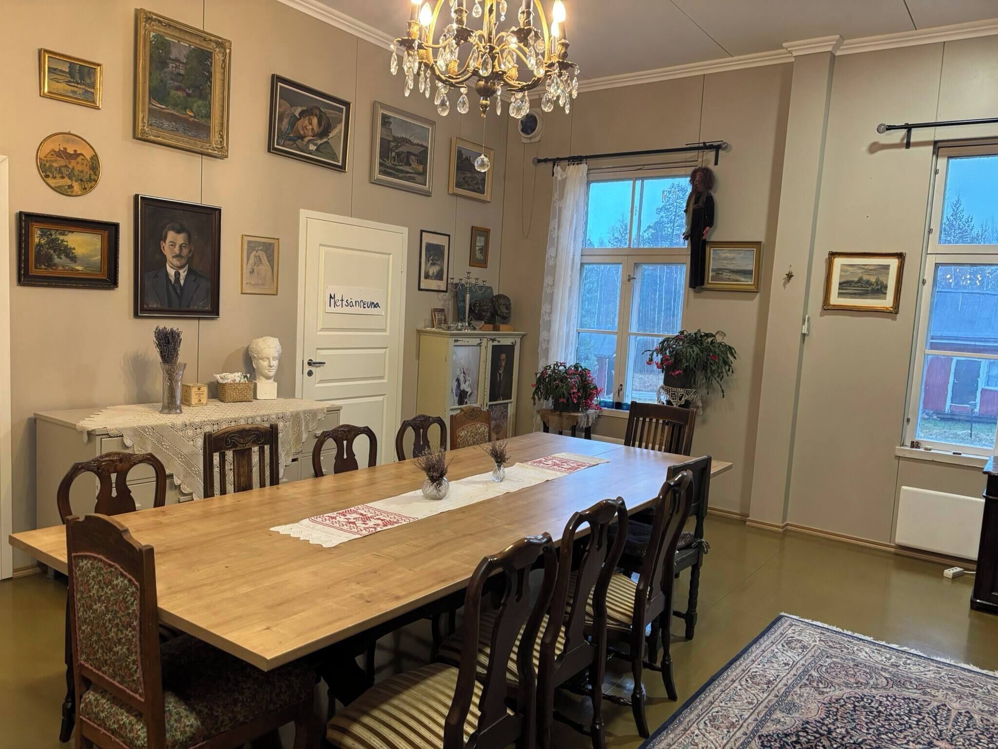 A dining room with a wooden table, chairs, a chandelier, and various framed pictures on the walls.