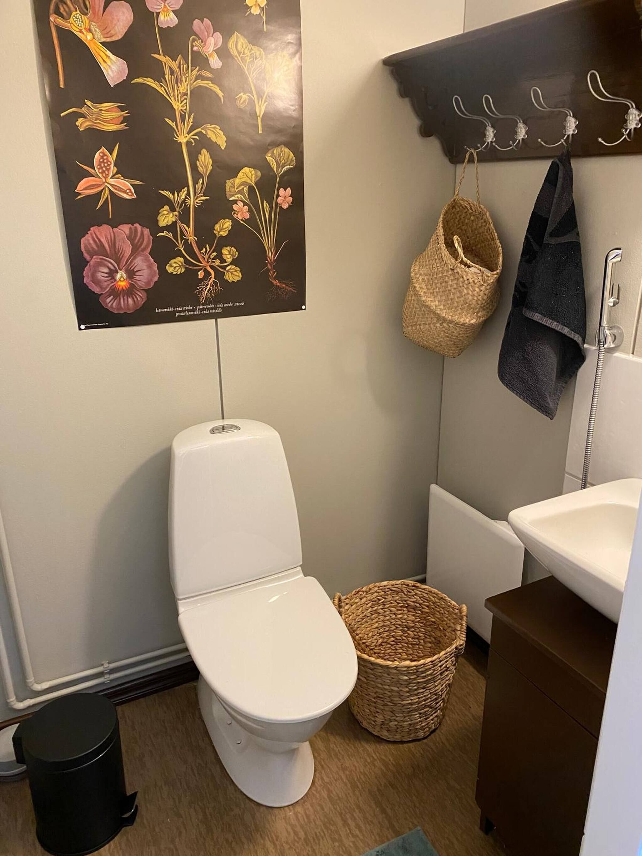 Ein Badezimmer mit Toilette, einem Korbwäschesessel, einem aufgehängten Handtuch und einem Wandhaken.
