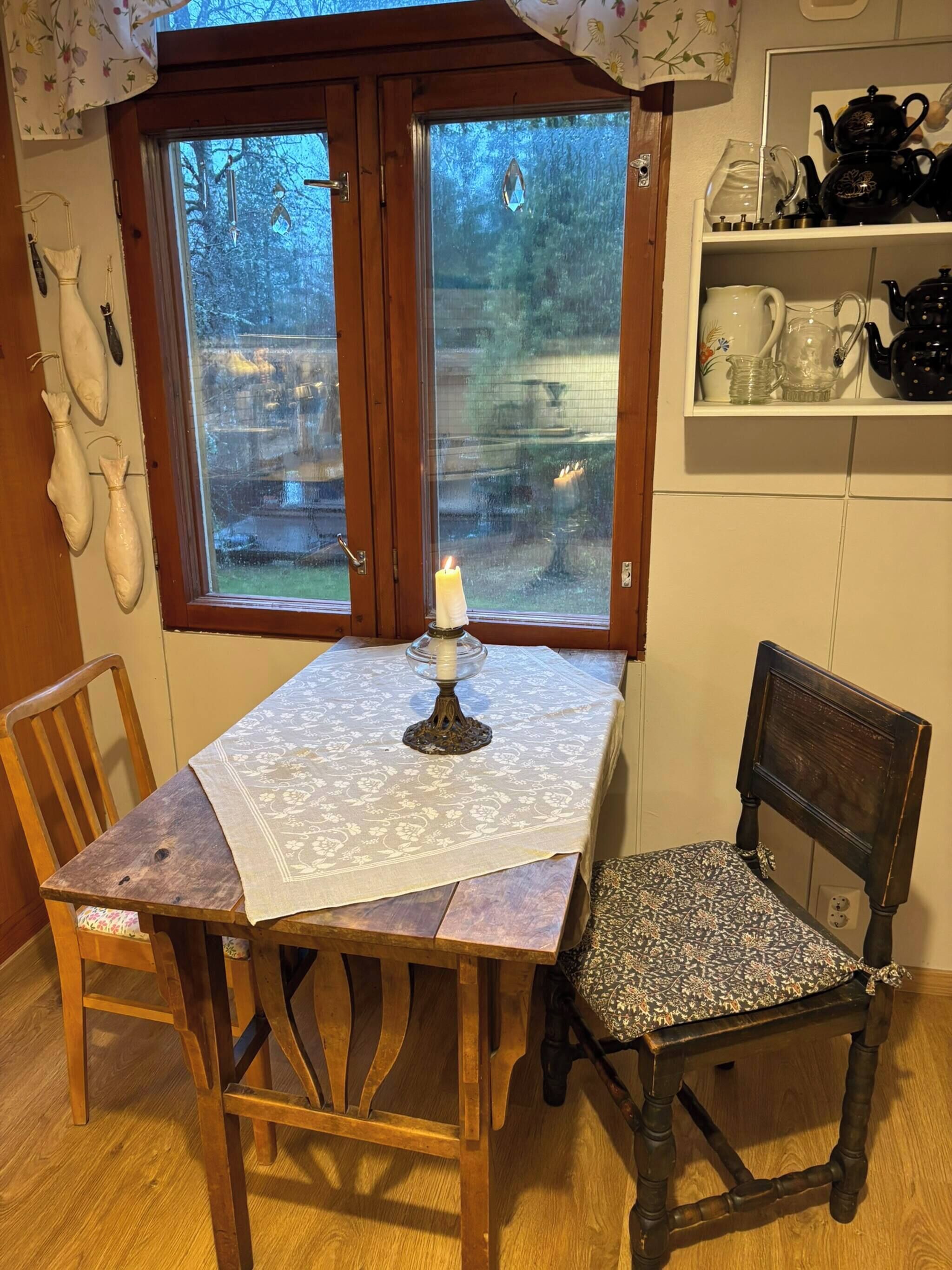 A wooden dining table with a white tablecloth, a candle, and two chairs.