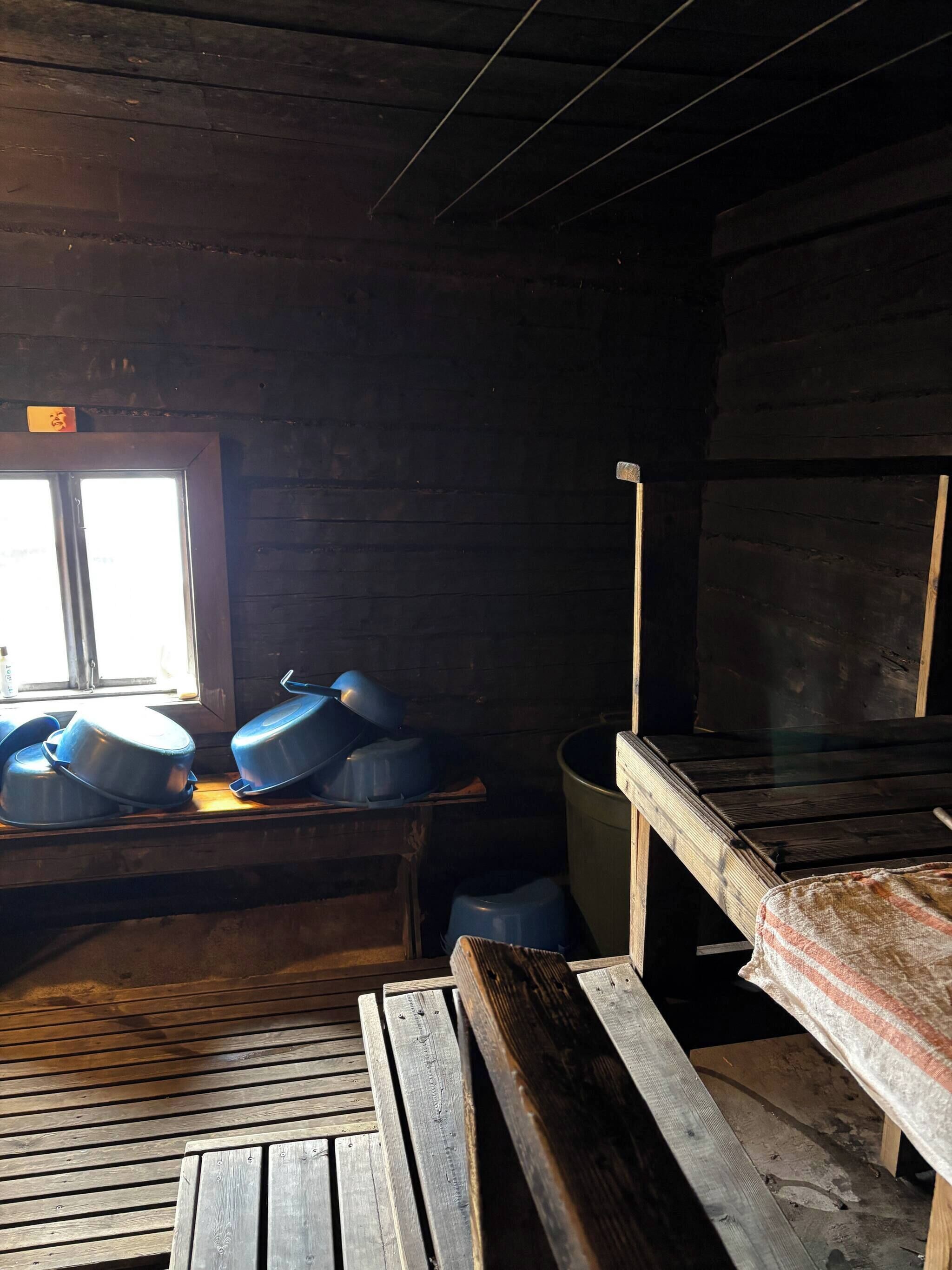A rustic cabin interior with a wooden bench, a window, and a table with blue containers.
