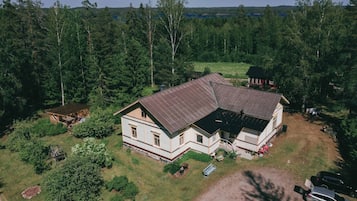 A two-story house with a sloped roof, surrounded by dense forest.