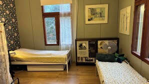 A room with two single beds, a small table, a framed picture, and a window with curtains. - Yöveden Ateljeekoti (Mikkeli)