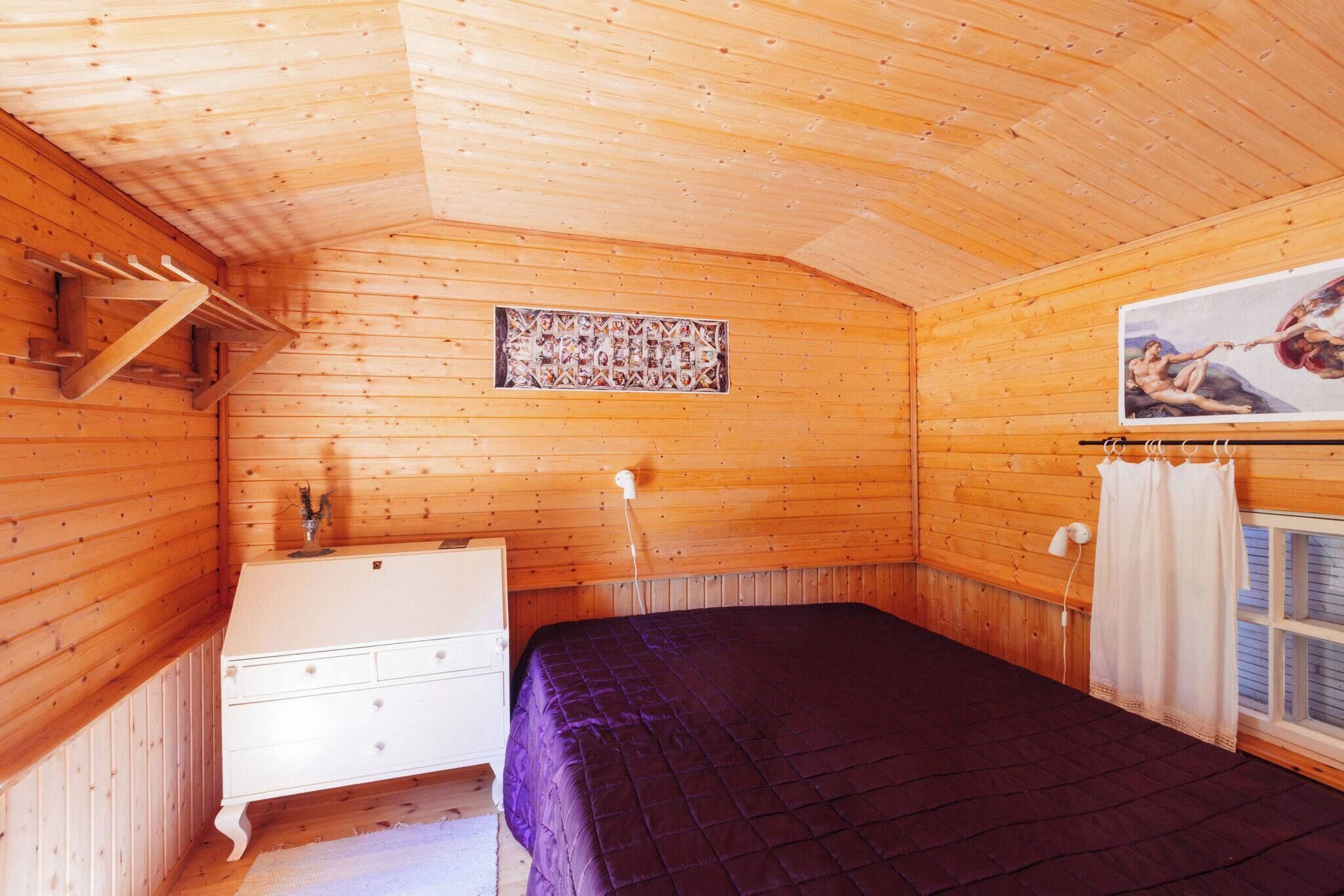 A wooden cabin room with a bed, dresser, and a painting on the wall.