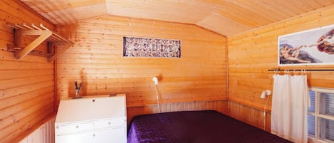 A wooden cabin room with a bed, dresser, and a painting on the wall.