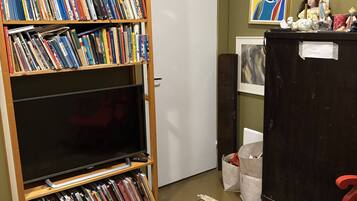 A room with a large bookshelf filled with books, a television on a stand, a patterned rug, and a red chair.