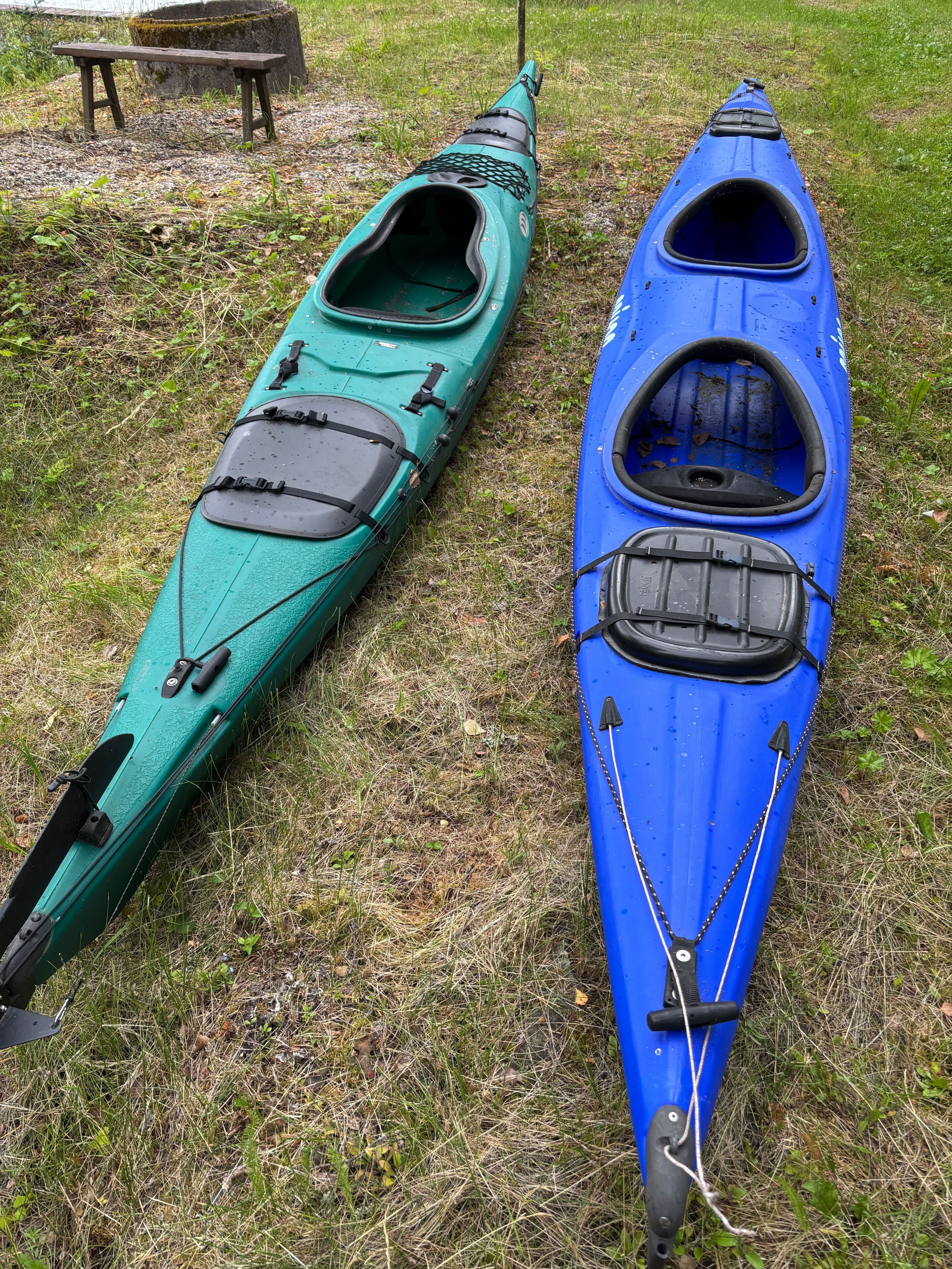 Two kayaks on a grassy field with a wooden bench in the background.