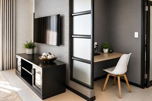 Una sala de estar moderna con televisor, un escritorio de madera, una silla blanca y una consola decorada con objetos ornamentales.