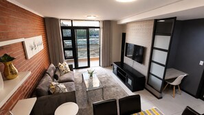 A modern living room with a sofa, coffee table, TV, and a dining area. - Luxury, safety and Convenience in the heart of Rosebank, Johannesburg!.. (Johannesburg)
