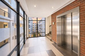 A corridor with a glass wall, a brick wall, and an elevator. - Luxury, safety and Convenience in the heart of Rosebank, Johannesburg!.. (Johannesburg)